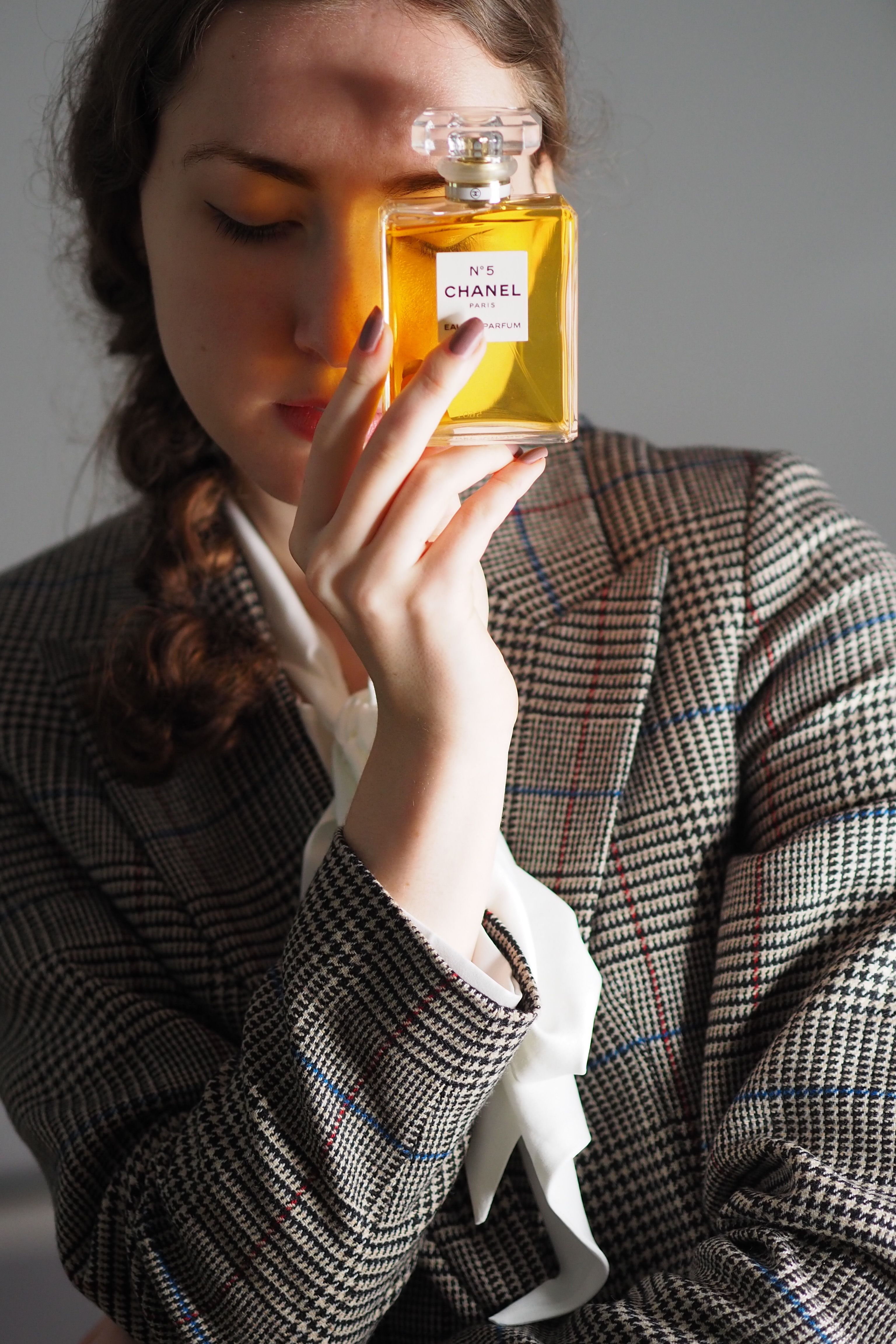 Caucasian woman holding Chanel perfume bottle in a stylish portrait.