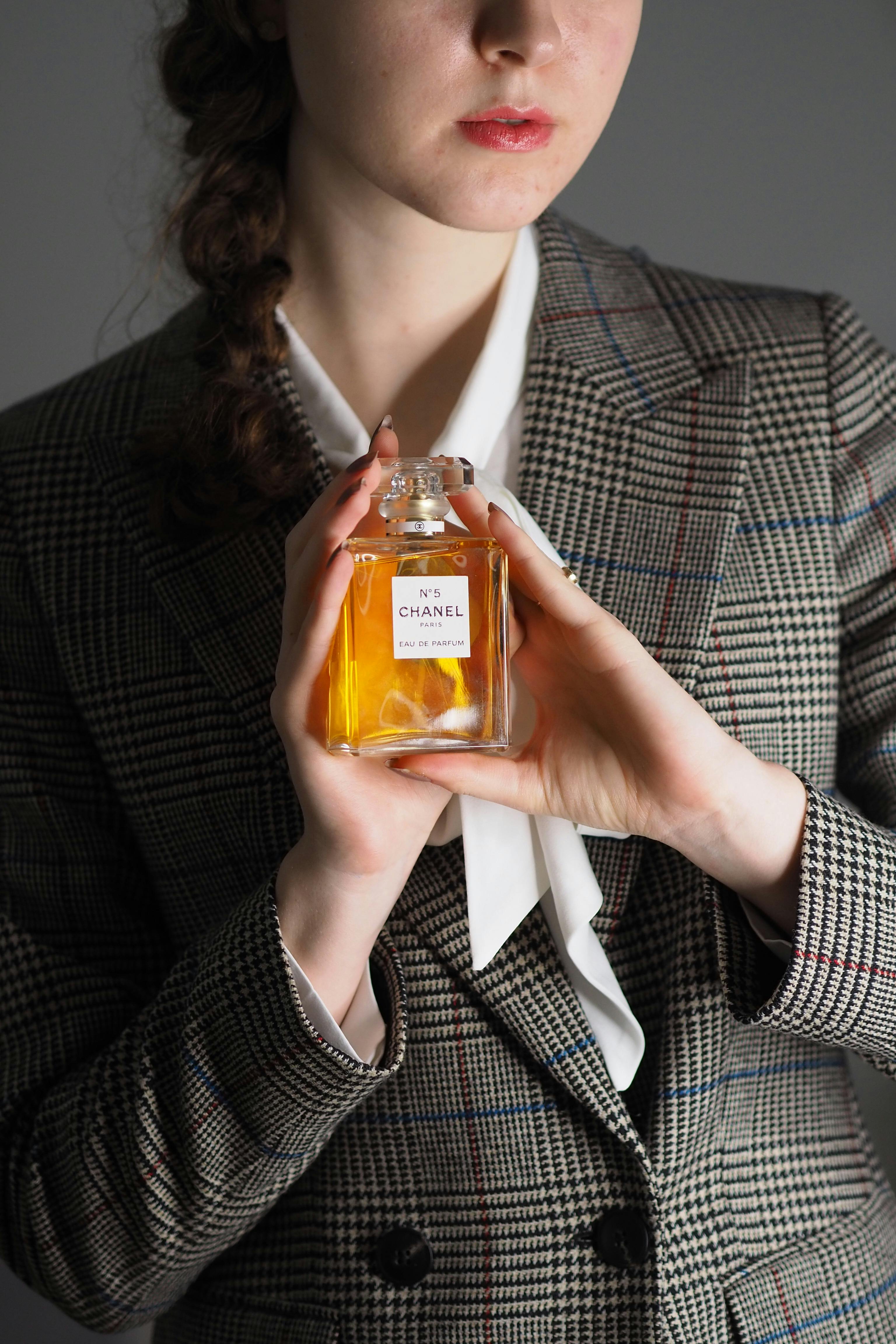 A young woman in a checkered blazer holds a luxury perfume bottle, showcasing elegance and style.