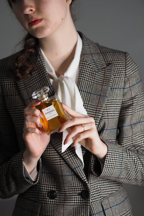 A woman in a suit holding a bottle of perfume