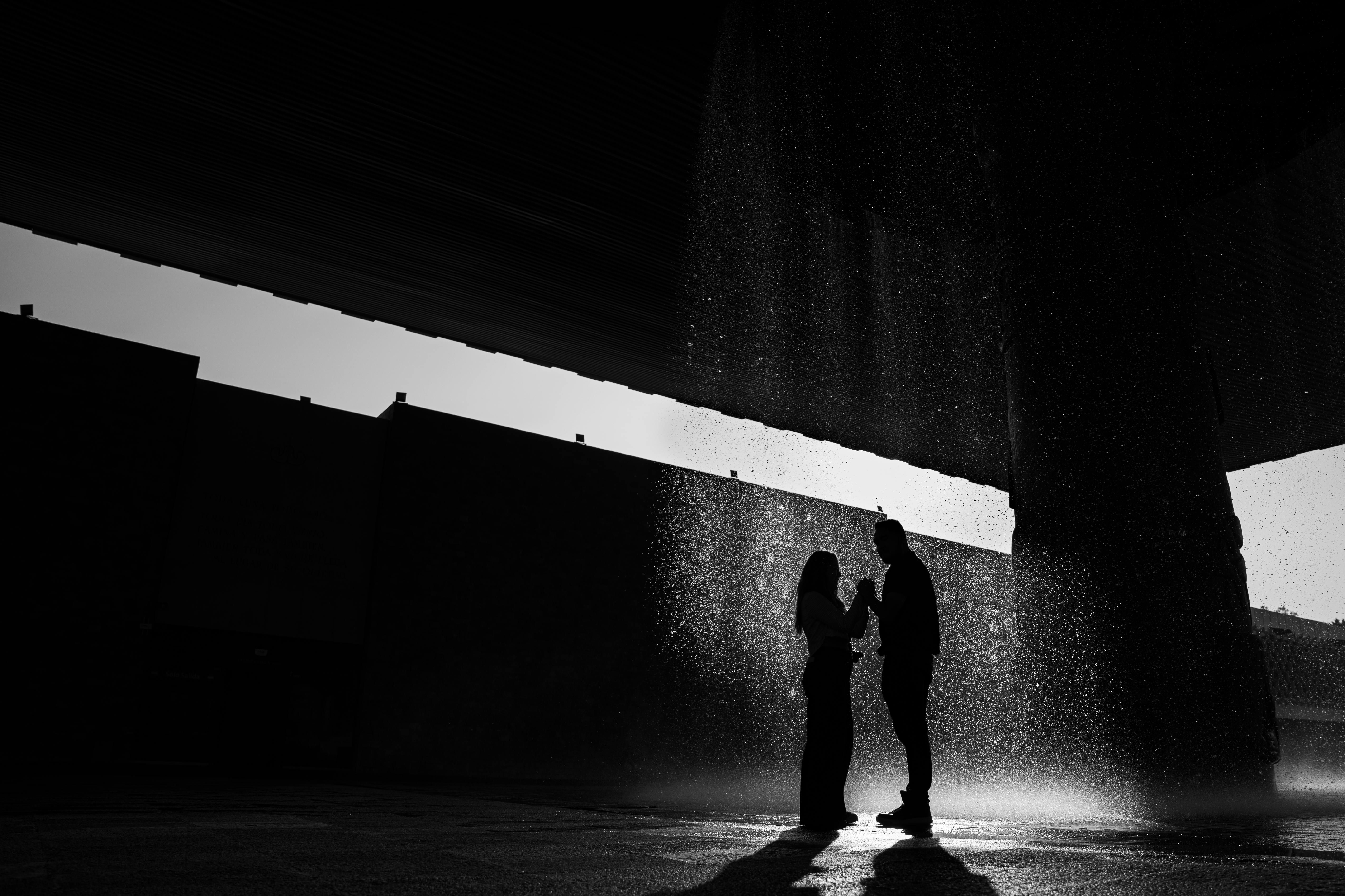 Silhouettes of two people standing intimately together in the rain, moody and romantic hypnotic embrace