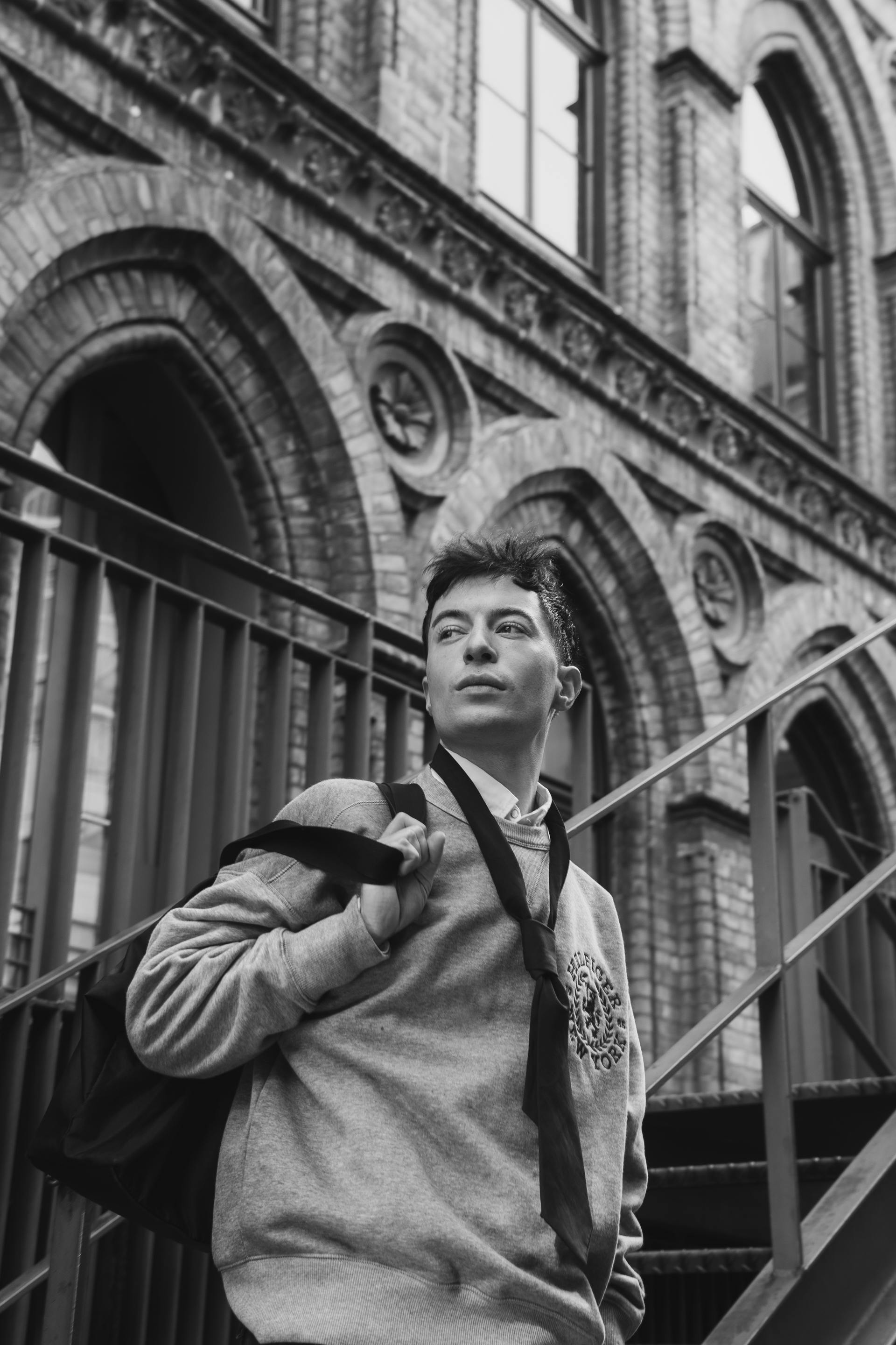 Stylish young man in a sweatshirt and necktie posing on a staircase, black and white.