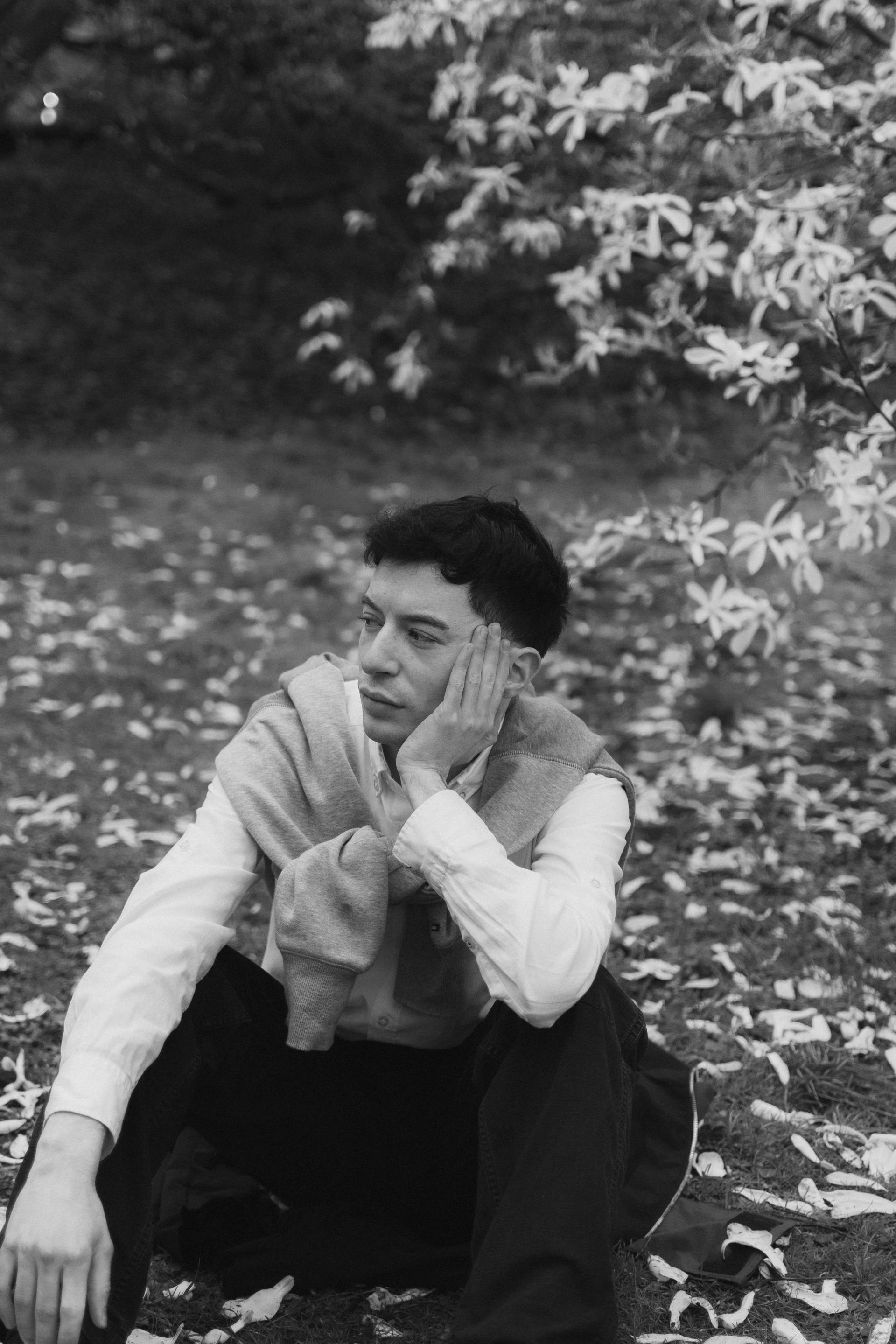 Black and white portrait of a young man sitting amidst fallen leaves outdoors, embodying a contemplative mood.