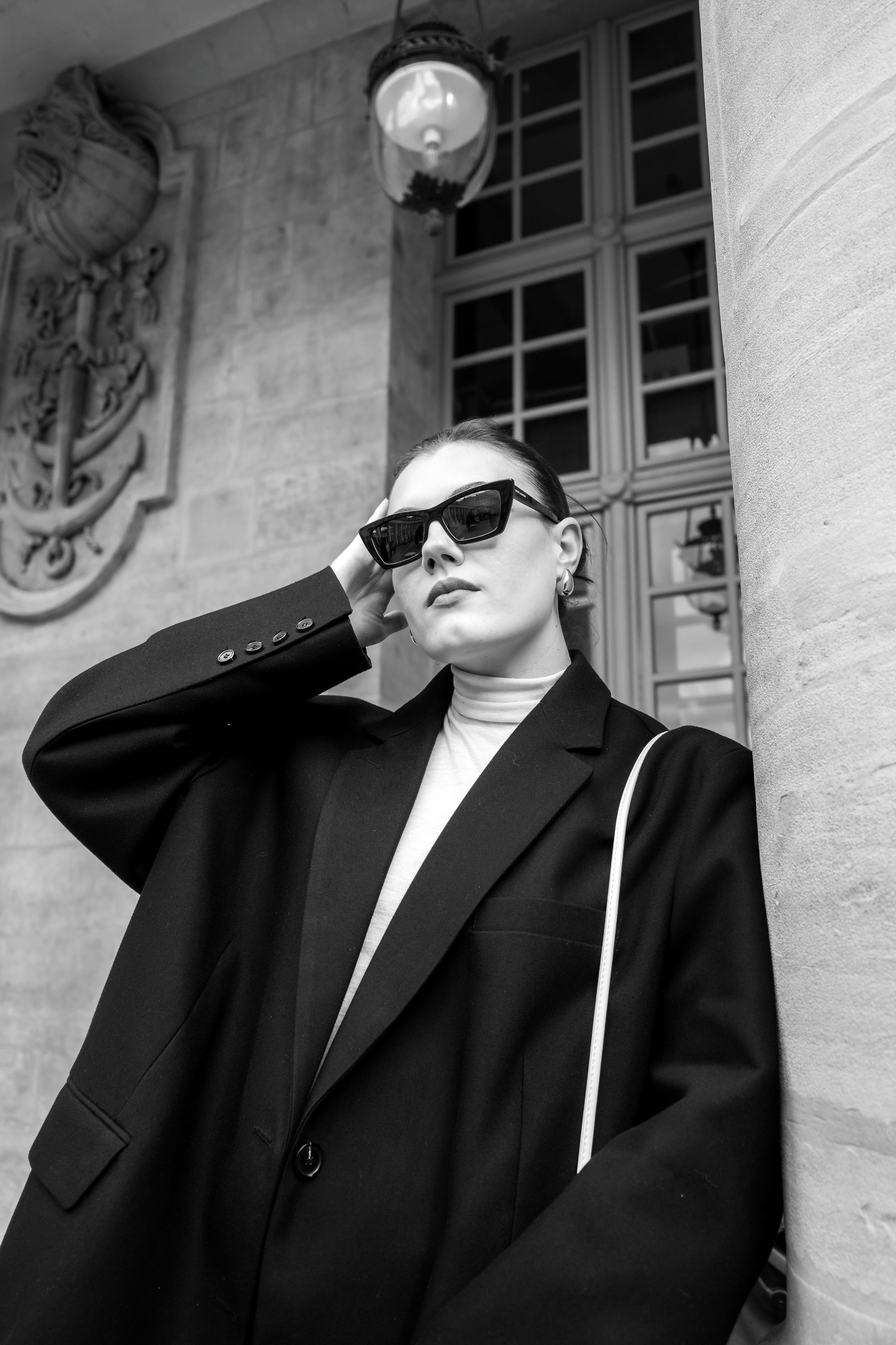 Black and white fashion portrait of a woman in sunglasses and blazer posing elegantly.