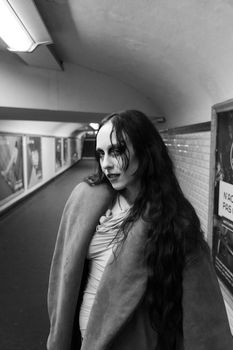 Striking black and white portrait of a woman with long hair and an overcoat in an urban subway tunnel.