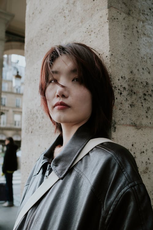 A woman in a leather jacket leaning against a wall