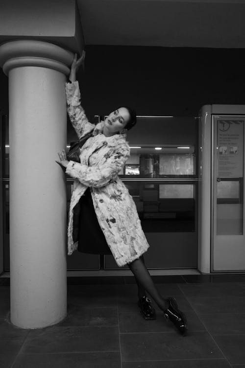 A woman leaning against a pillar in a coat