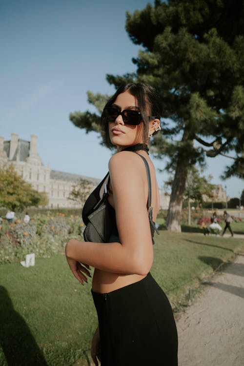 A woman in a black top and sunglasses standing in front of a park