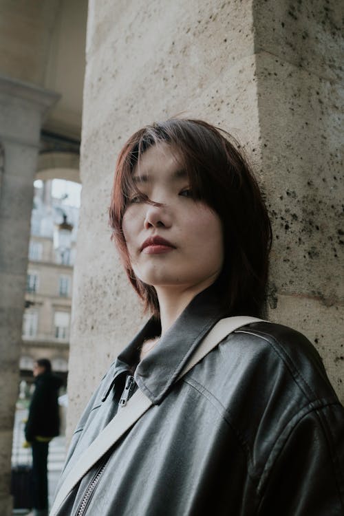 A woman in a leather jacket leaning against a pillar