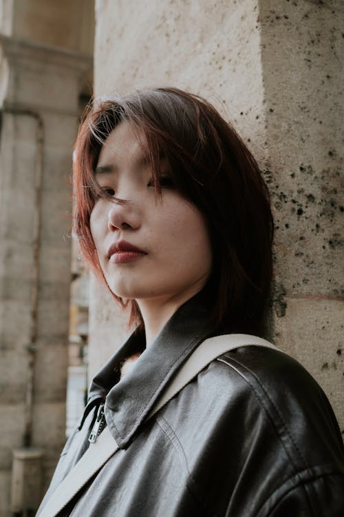 A woman in a leather jacket leaning against a wall