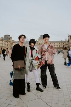 Trio posing stylishly in front of the Louvre, Paris art landmark.