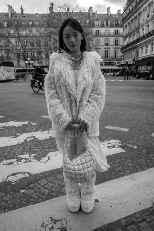 A woman in a white fur coat and boots standing on the street