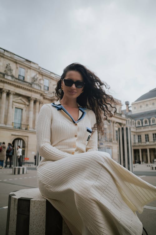 A woman in a white dress and sunglasses sitting on a bench