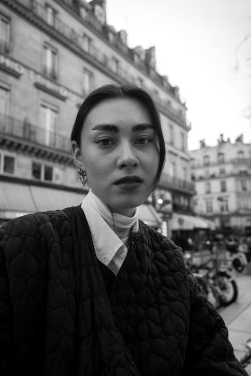 A woman in a jacket and scarf standing in front of a building