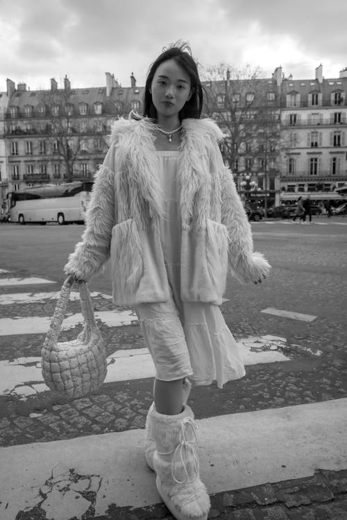A woman in a white fur coat and white boots crossing the street