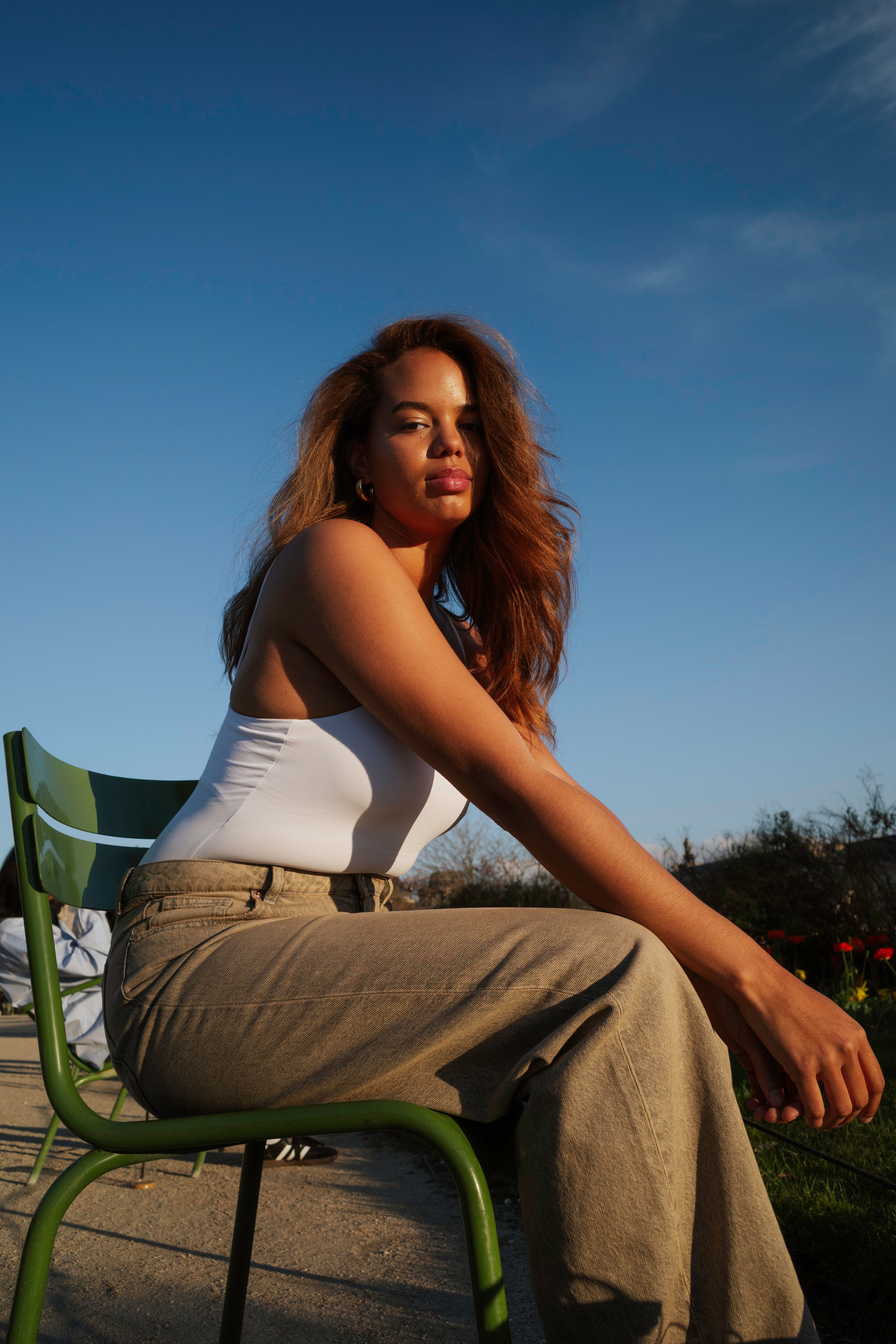 Portrait of a woman sitting on a green chair outdoors, enjoying the sunlight.