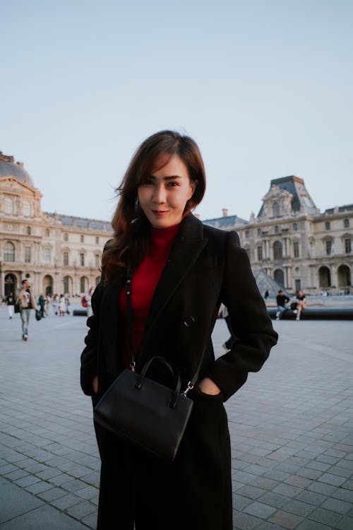 A woman in a red coat and black purse standing in front of a building