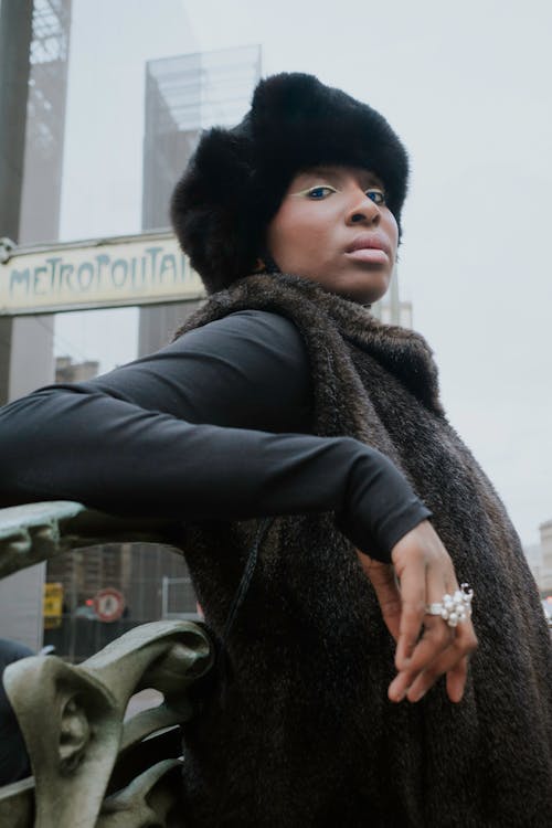 A woman in a fur coat leaning against a pole