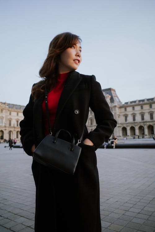 A woman in a red coat and black purse standing in front of a building
