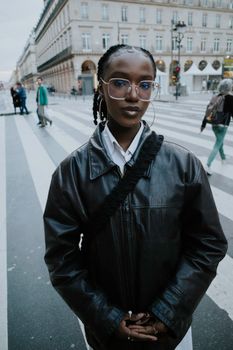 A fashionable woman in a black leather jacket standing confidently on an urban crosswalk.