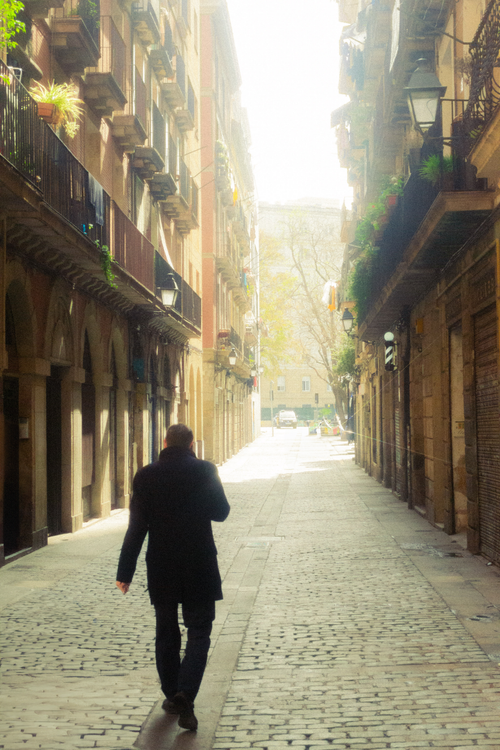 Free A man in a jacket walks down a sunlit cobblestone street in historic Barcelona, capturing urban life. Stock Photo