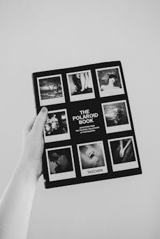 一张手持宝丽来照片书的单色图像，其中包含了各种照片
