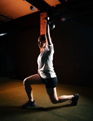 Overhead kettlebell lunge in a dimly lit gym. Photo by Franklin Santillan A. on Pexels