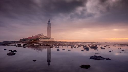 Free A captivating view of St Mary's Lighthouse at dusk with tranquil ocean reflections and dramatic clouds. Stock Photo