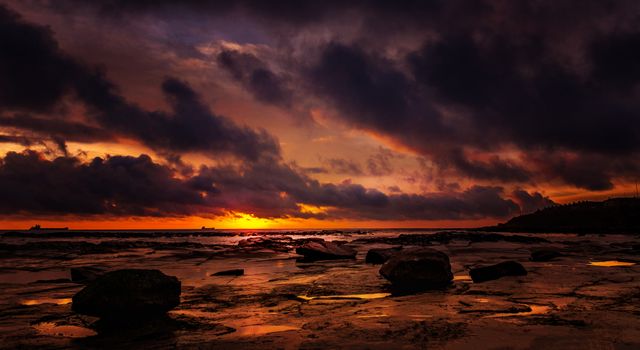Breathtaking sunset over a rocky shore with dramatic clouds and ocean view.
