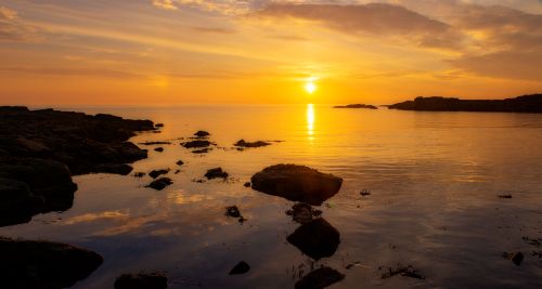 Free Beautiful sunset over a rocky coastline, showcasing vibrant colors and serene reflections. Stock Photo