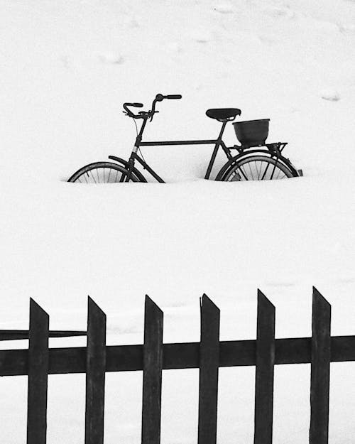 A bicycle is buried in the snow behind a fence
