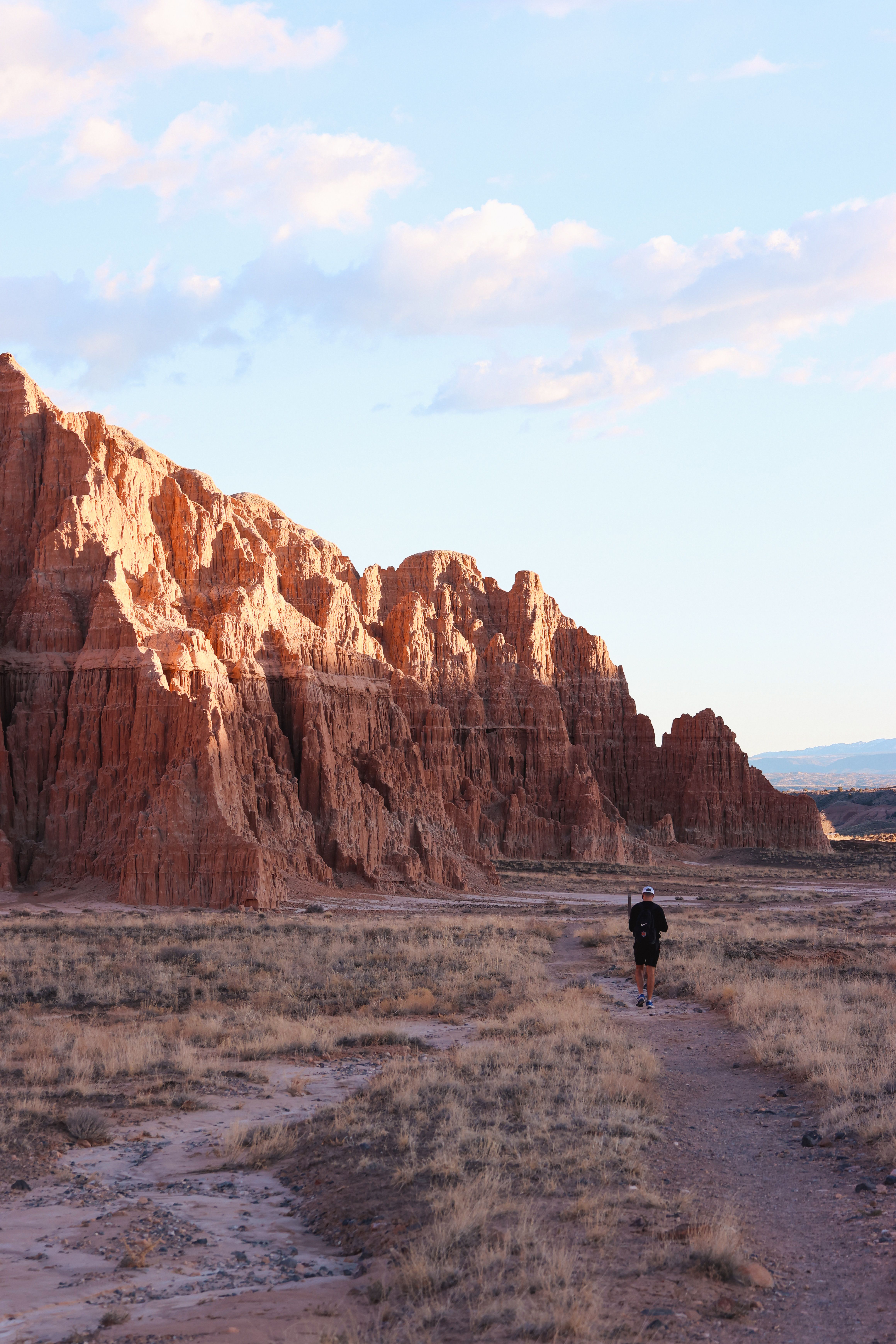 Hiker on a trail in Cathedral Gorge, showcasing stunning rock formations at sunset.