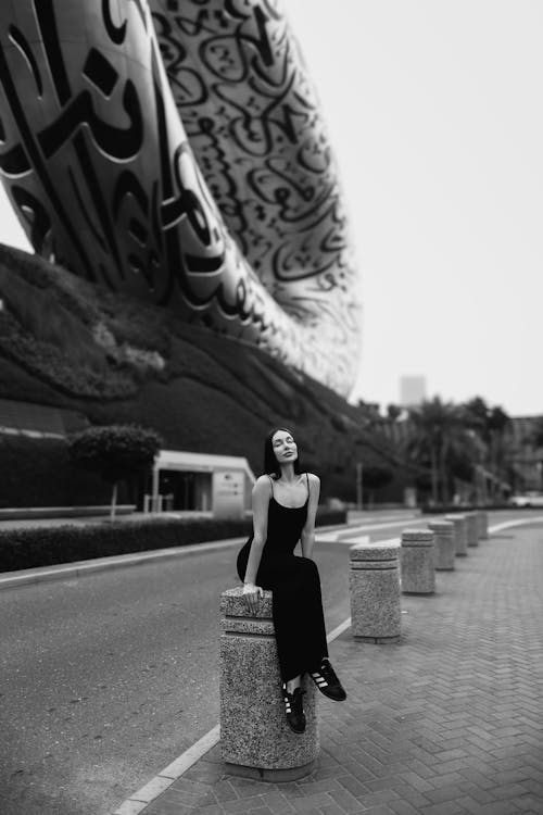 Woman in Dress Sitting by Road with Modern Building behind