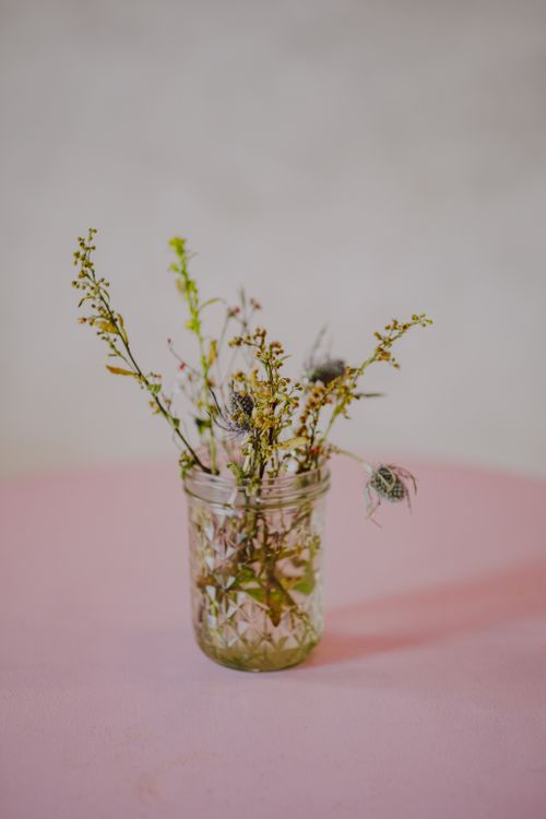 Free Aesthetic display of delicate wildflowers in a textured glass jar on a pink surface. Stock Photo
