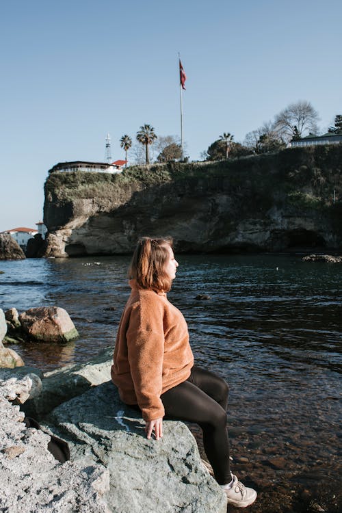 A woman sitting on rocks near the water