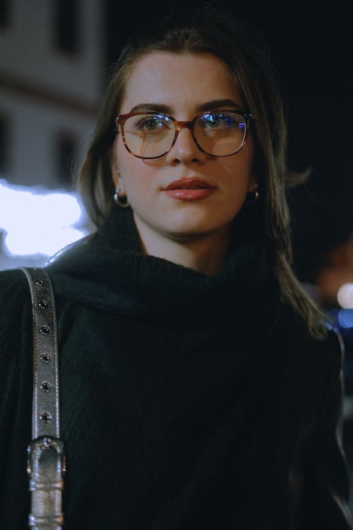A woman wearing glasses and a black coat at night
