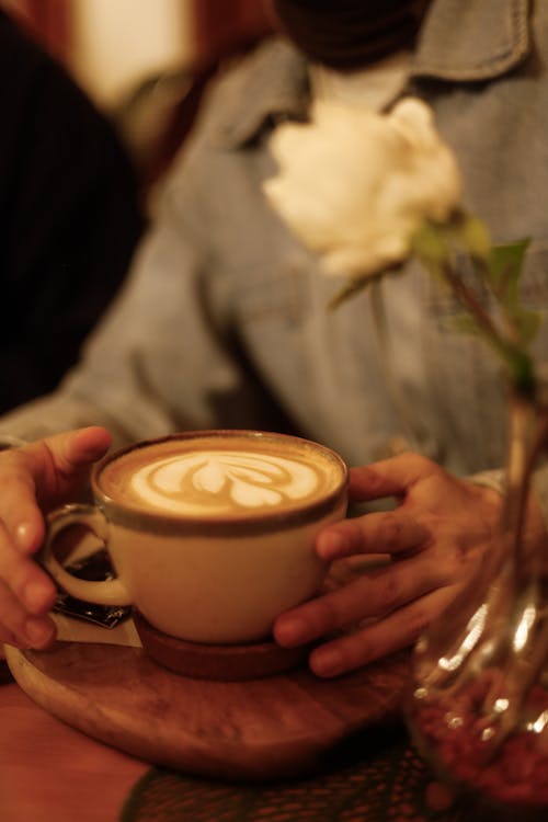 Free A person holding a cup of coffee with a flower on top Stock Photo
