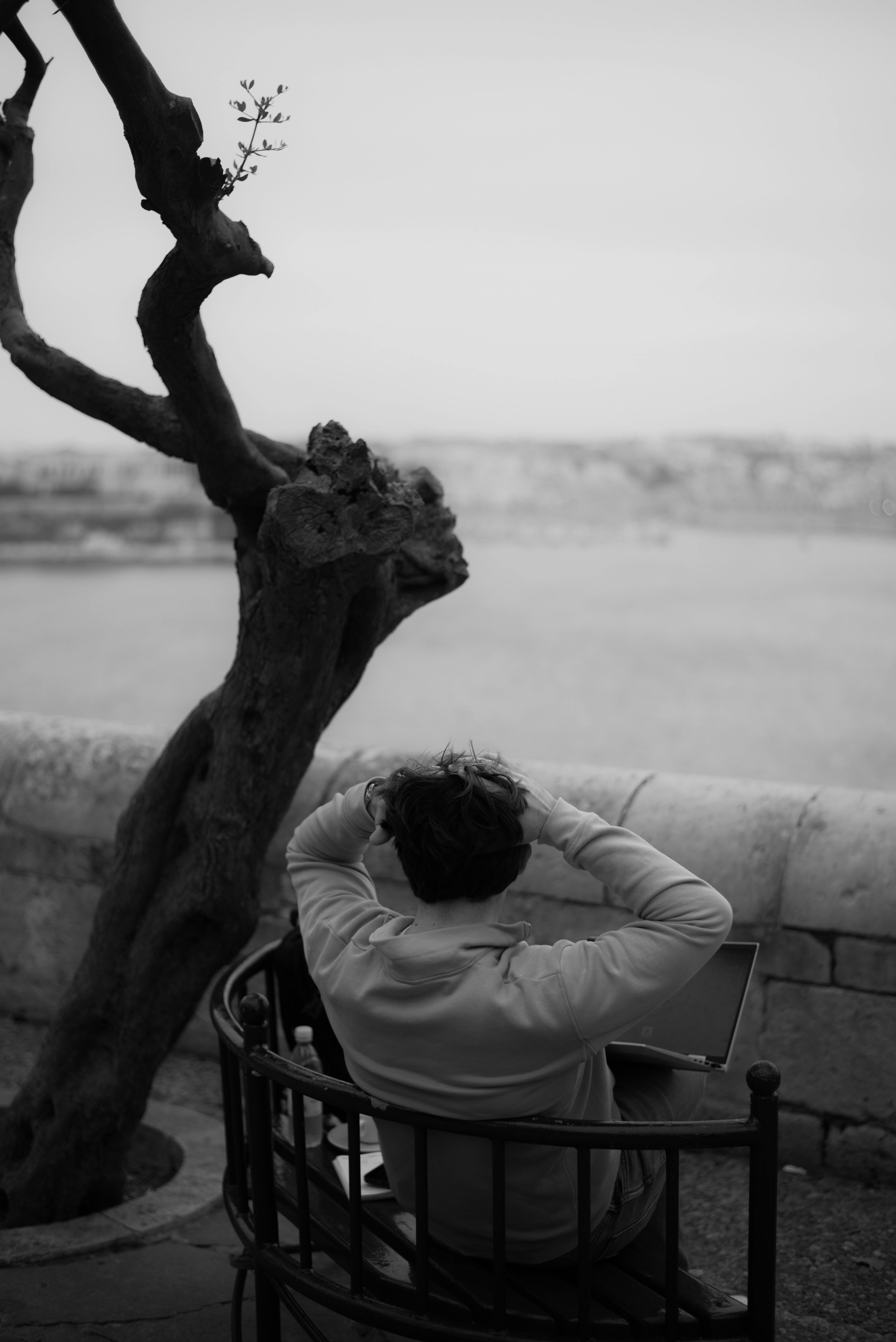 A person sitting by a river, reflecting quietly with a laptop in monochrome.