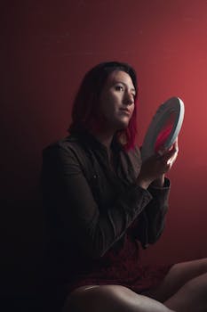 在喜怒无常的红色背景下，红头发的女人拿着镜子