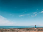 一个人站在田野里，俯瞰着广阔的海洋和湛蓝的天空，感受着夏日的氛围