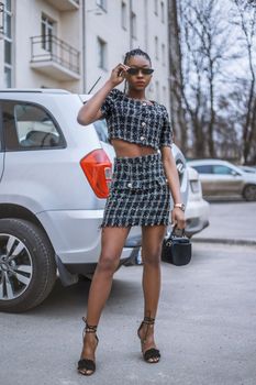 Stylish woman in tweed set and sunglasses, posing in urban Ukraine setting.