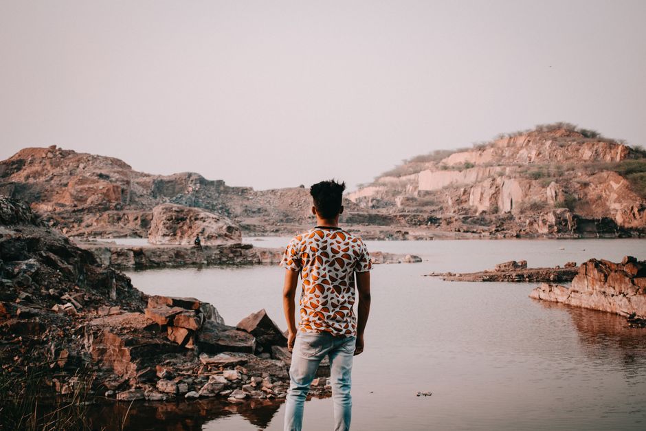A man in a patterned shirt stands by a rocky lake, enjoying the serene summer view.