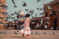 一个年轻女孩在历史悠久的户外环境中，快乐地与飞鸽嬉戏，捕捉到了欢乐与纯真的瞬间