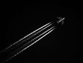 高对比度的黑白图像中，飞机在夜空中留下凝结尾迹