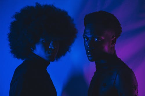 Two people with afro hair standing in front of a purple light