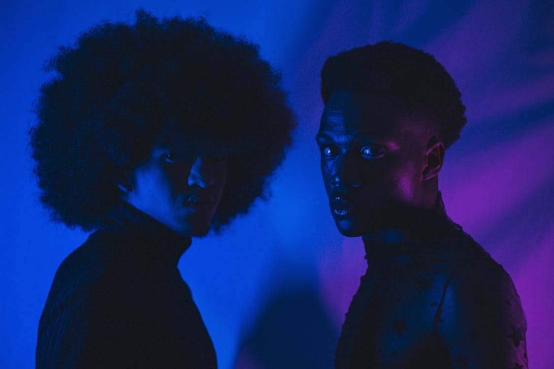 Two people with afro hair standing in front of a purple light