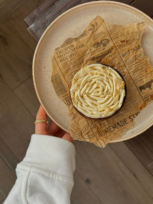 Free Close-up of a hand holding a cream-topped pastry on a rustic paper plate. Stock Photo