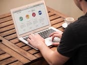 在户外用笔记本电脑打字的人们，展现了在木桌旁喝咖啡的远程工作生活方式