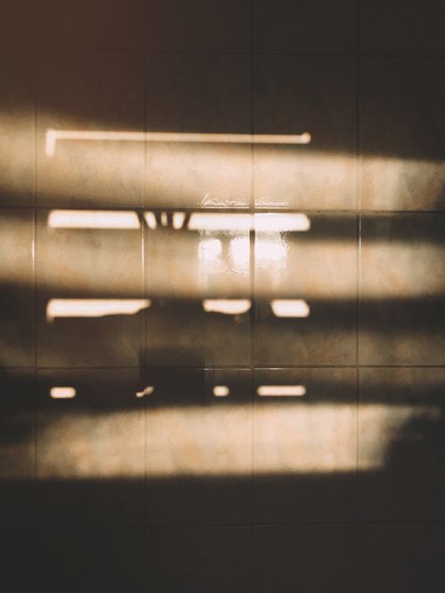 Free Sunlight creating abstract patterns through blinds, casting shadows indoors on a tiled wall. Stock Photo