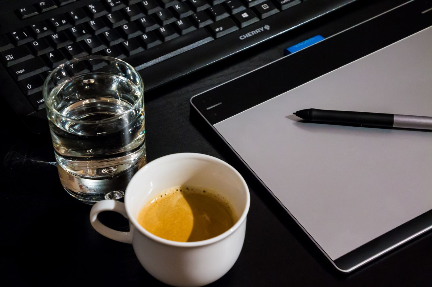 Office desk setup with a coffee cup, glass of water, tablet, pen, and keyboard.