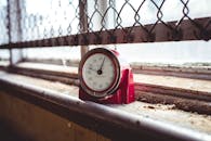 一个红色的计时器放在尘土飞扬的窗台上，背景是链节围栏，唤起怀旧之情